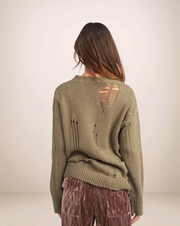 Person wearing a green sweater with cut-out design on a plain background