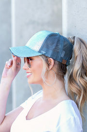 Woman wearing a blue trucker cap and sunglasses against a light gray wall.