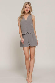 a blonde woman modeling a pair of gray pleated tailored shorts with a matching vest