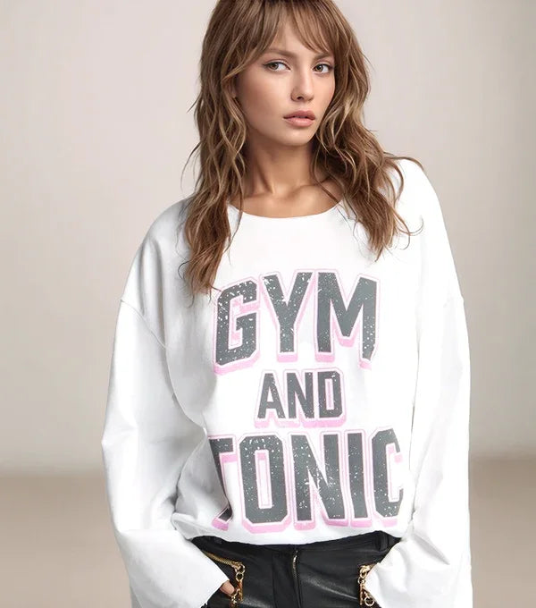 Woman wearing a white sweatshirt with 'GYM AND TONIC' text on a beige background