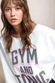 Woman wearing a white sweatshirt with 'GYM AND TONIC' text