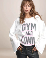 Woman wearing a white sweatshirt with 'GYM AND TONIC' text on a beige background