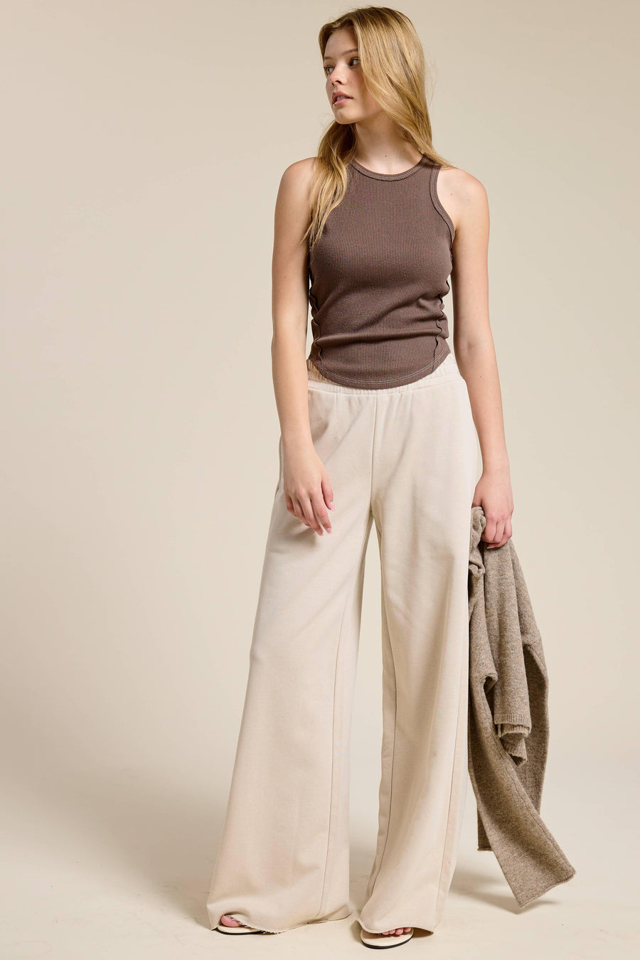 Woman wearing a sleeveless brown top and beige wide-leg pants against a plain background