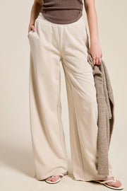 Person wearing beige wide-leg pants holding a brown jacket against a plain background