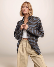 Woman wearing a plaid shirt over a white top and beige pants on a plain background