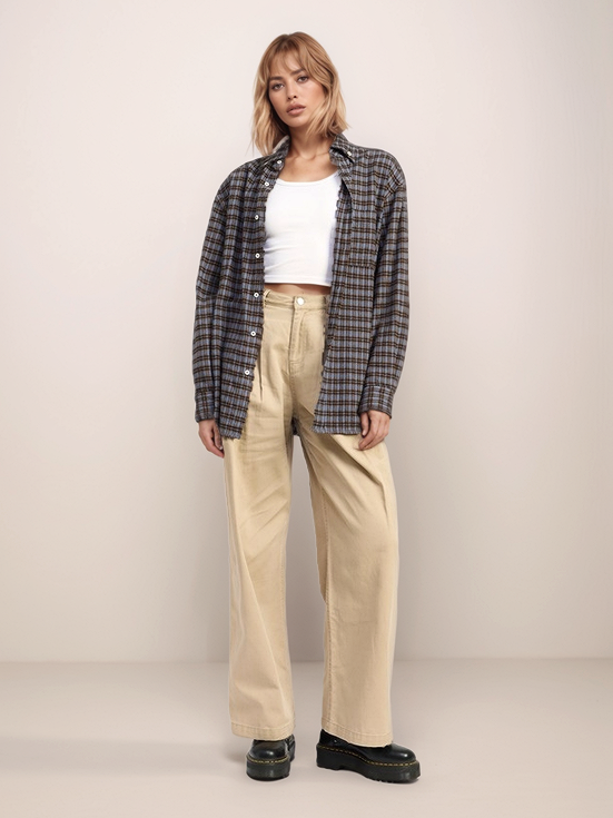 Person wearing a plaid shirt, white top, beige pants, and black shoes on a plain background