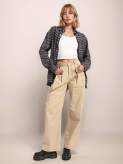 Person wearing a plaid shirt, white top, beige pants, and black shoes on a plain background