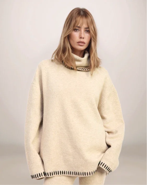 Woman wearing a cream-colored sweater with a high collar against a plain background