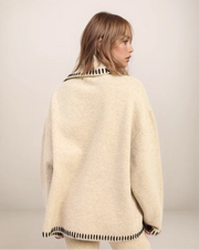 Woman wearing a beige poncho with black trim on a plain background