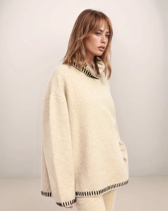 Woman wearing a cream-colored sweater with black and white striped trim on a plain background