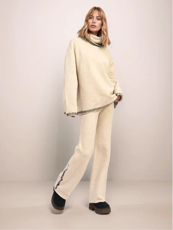 Person wearing a cream-colored outfit with a turtleneck sweater and pants on a plain background