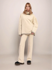 Person wearing a beige sweater and pants set on a plain background