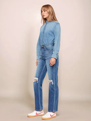 Woman wearing a denim outfit with ripped jeans on a beige background