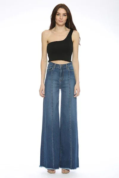 Woman wearing a black one-shoulder top and dark blue wide-leg jeans on a white background