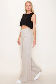 Woman wearing a black sleeveless top and beige wide-leg pants on a plain background