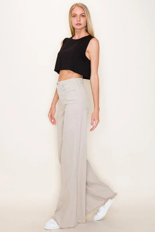 Woman wearing a black sleeveless top and beige wide-leg pants on a plain background