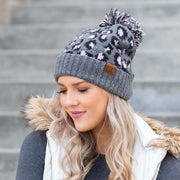 Woman wearing a gray patterned beanie with a pom-pom on a blurred background