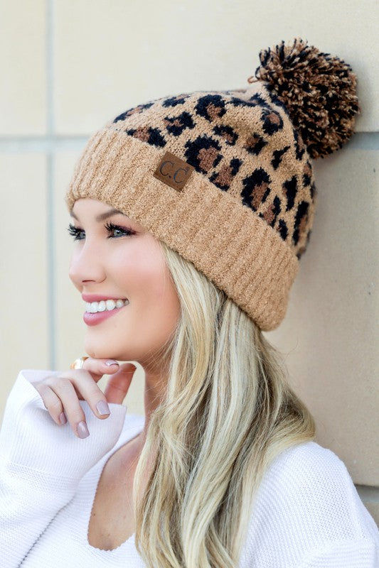 Woman wearing a leopard print beanie with a pom-pom against a neutral background