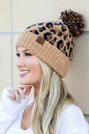 Woman wearing a leopard print beanie with a pom-pom against a neutral background
