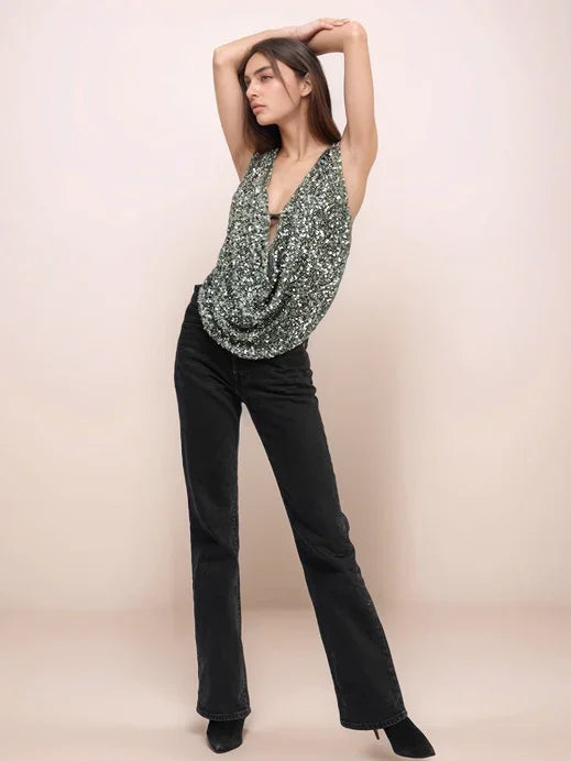 Woman wearing a green patterned top and black pants against a beige background