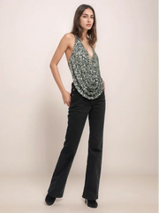 Woman wearing a sleeveless patterned top and black pants on a beige background