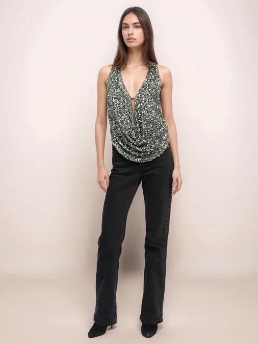 Woman wearing a sequined top and black pants on a plain background