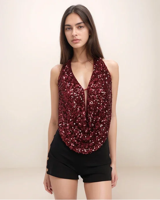 Model wearing a maroon sequin top and black shorts on a beige background