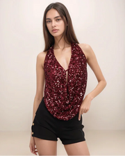 Woman wearing a sparkly red top and black shorts on a plain background