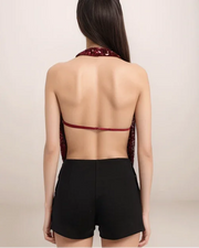 Woman wearing a red open-back top and black shorts on a beige background