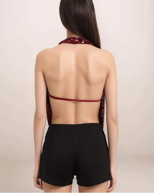 Woman wearing a red open-back top and black shorts on a beige background