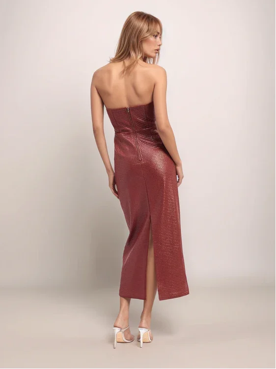 Woman wearing a strapless, burgundy evening gown with a slit on a plain background