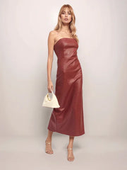 Woman wearing a strapless red dress holding a white handbag against a plain background