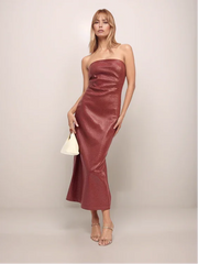 Woman wearing a strapless red dress holding a white handbag against a plain background