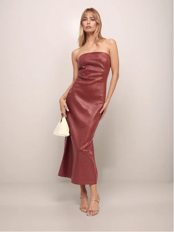 Woman wearing a strapless red dress holding a white handbag against a plain background