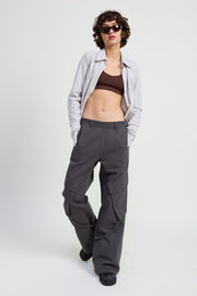 Woman wearing a striped shirt, brown top, and gray cargo pants on a white background