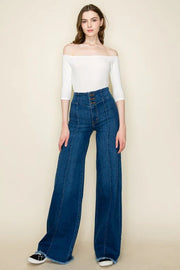 Woman wearing a white off-shoulder top and blue jeans on a beige background