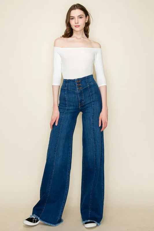 Woman wearing a white off-shoulder top and blue jeans on a beige background