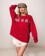 Person wearing a red sweatshirt with 'MERRY' text, white shorts, and a cap on a plain background