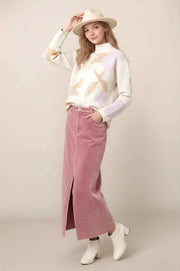 woman wearing an abstract floral sweater with a pink maxi skirt, booties and a hat.