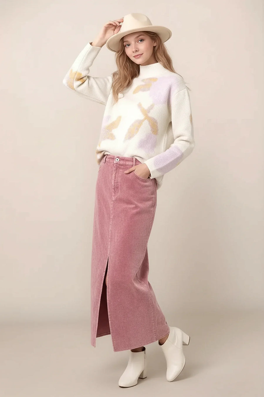 woman wearing an abstract floral sweater with a pink maxi skirt, booties and a hat.