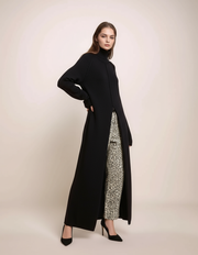 Woman wearing a long black coat over a patterned dress on a beige background