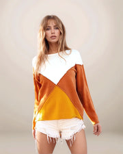 Woman wearing a color-blocked sweater with white, orange, and yellow sections on a plain background.