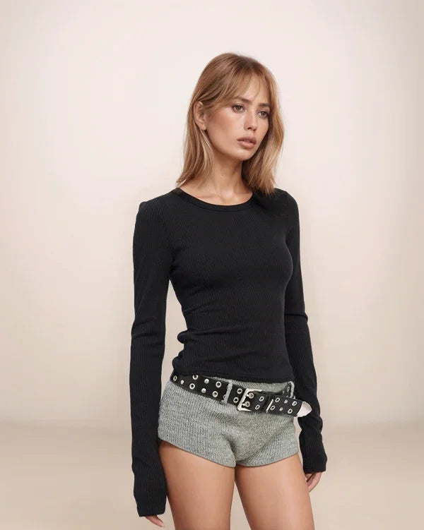 Woman wearing a black long-sleeve top and gray shorts with a belt against a beige background