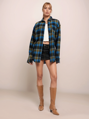 Woman wearing a plaid shirt, black skirt, and tan boots on a beige background