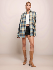 Woman wearing a plaid shirt, white top, black shorts, and tan knee-high boots on a plain background