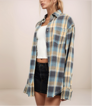 Person wearing a plaid shirt over a white top and black shorts on a plain background