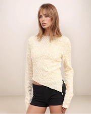 Woman wearing a white sequin sweater and black shorts against a plain background