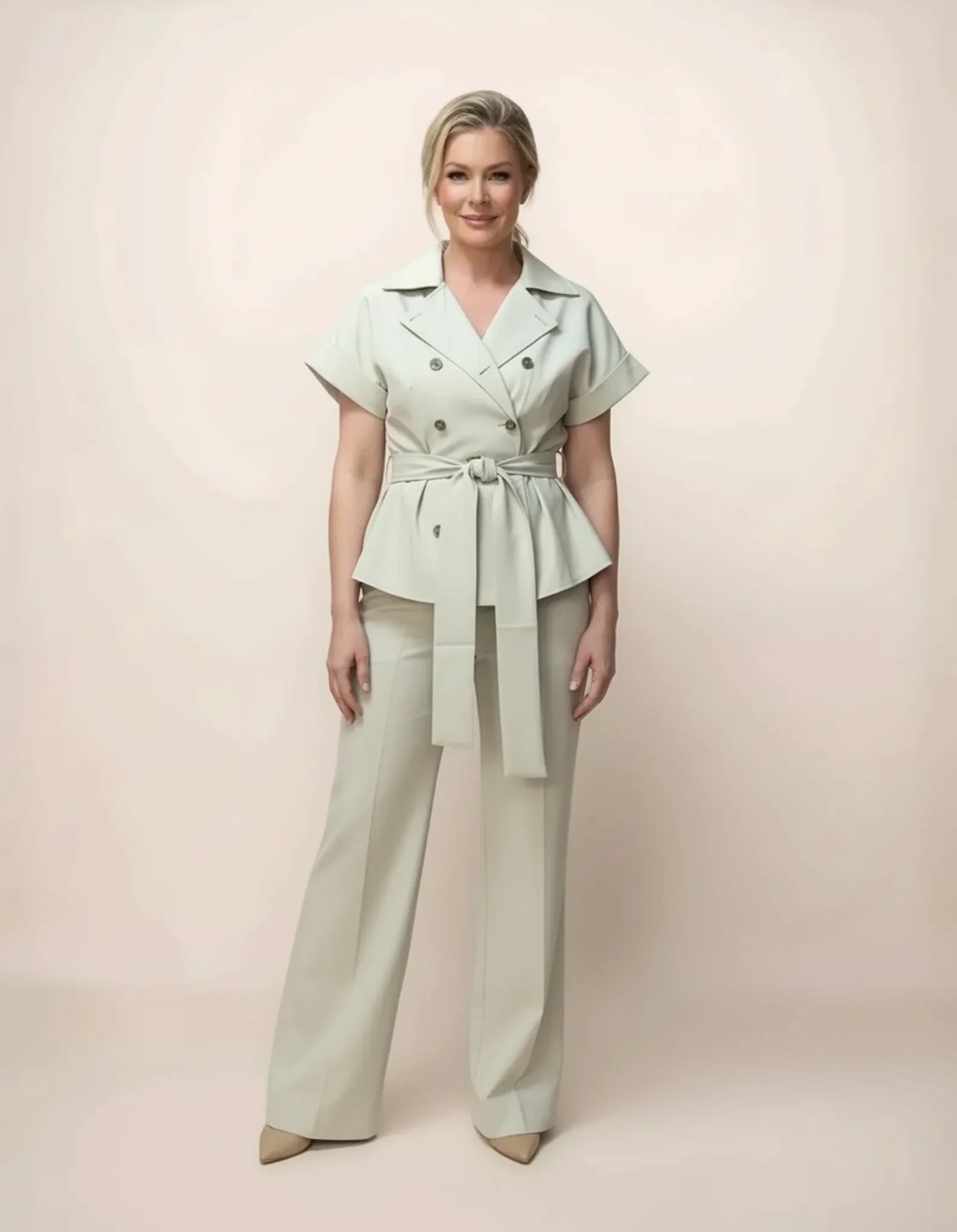 Woman wearing a light green peplum top and beige pants against a plain background