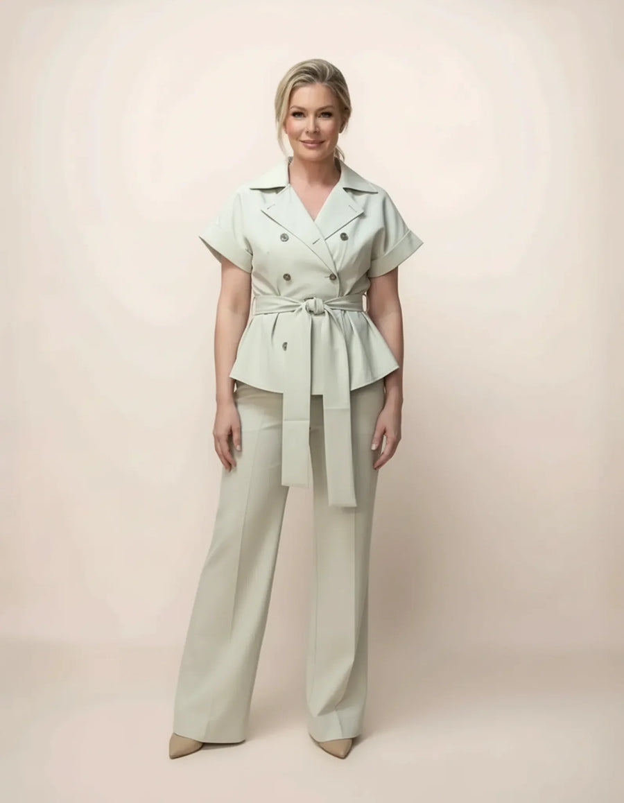 Woman wearing a light green peplum top and beige pants against a plain background