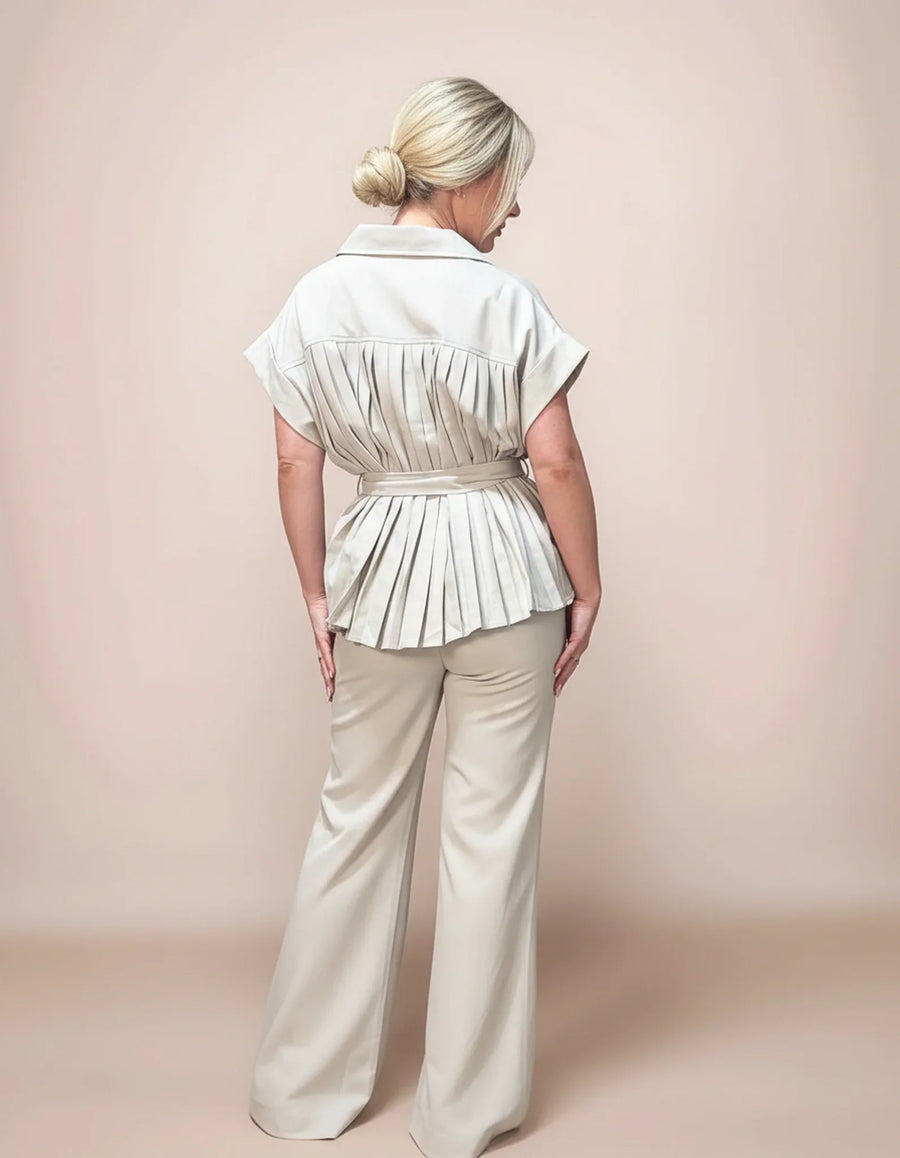 Woman wearing a light-colored peplum top and wide-leg pants against a plain background